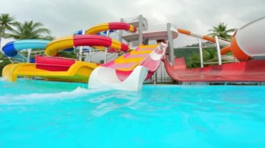 Renkli su kaydırağının geniş bir görüntüsü, Tayland 'da bir kızın kayması ve gündüz vakti havuzda su sıçratması.