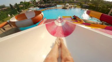 Bir fpv pov, Tayland 'da bir su parkında kırmızı ve beyaz bir su kaydırağından kayarak yüzen ve gündüz vakti yüzen birinin bacaklarını gösteriyor.