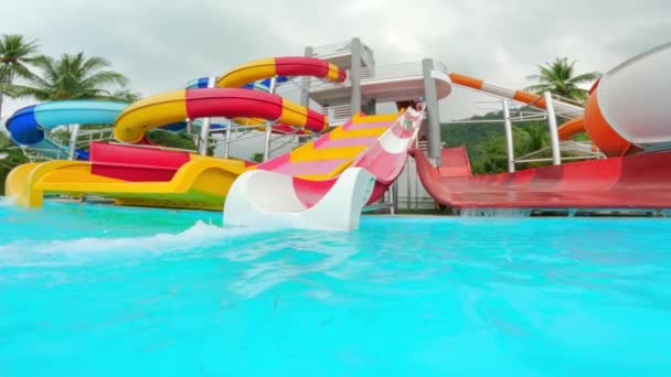 タイの昼間にプールで少女がスライドし 水しぶきとカラフルな水のスライドの広いショット — ストック動画