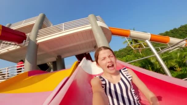 一名女孩手持相机拍摄自己的照片 同时滑下红色和白色的滑梯 然后在随后的一天 在泰国的一个水上公园里飞溅进了一个游泳池 — 图库视频影像