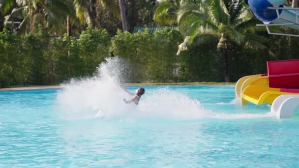 タイのウォーターパークのスイミングプールに飛び散るスライドからカメラを持っている女の子のビデオ — ストック動画
