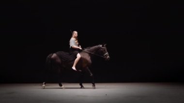 Genç Savaşçı Kadın Zincirli Giyinik ve Elinde Kılıçla Stüdyoda Siyah Arkaplan Karşısında At Biniyor. Horse Walks Around a Circle 'da. Yavaş Hareket Görüntüsü