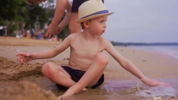タイの昼間 砂の上に座って海岸で水遊びをする少年のビデオ — ストック動画