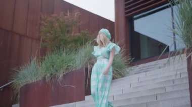 Sarışın bir kadın, kareli bir akuamarin elbisesi ve örgü beresi giyiyor, moda çekimi sırasında aşağıya iniyor.