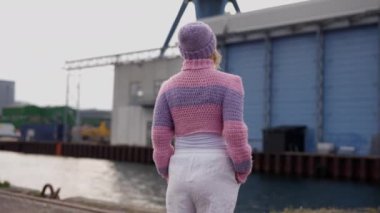 Sıcak pembe ve mor yün bir kazakla sarılı kadın binaya ve gökyüzüne bakıyor.
