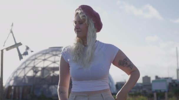 一位穿着白衬衫 头戴粉色贝雷帽的金发女子的中影正在消退 她向左望着 白天她身后有一个大地测量穹顶 — 图库视频影像