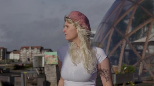 在阳光灿烂的日子里 一位身穿白衬衫 头戴粉色贝雷帽的金发女子站在大地测量圆顶附近的中景照片 — 图库视频影像