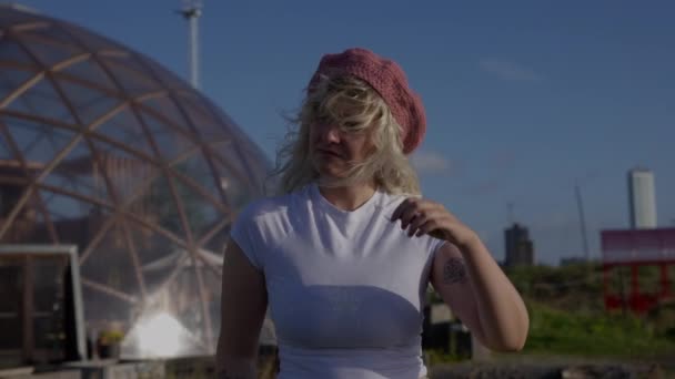 一只中等镜头冲向一位穿着白衬衫 站在大地测量圆顶附近的金发女子 她在多风的天气里把头发和粉色贝雷帽固定好了 — 图库视频影像