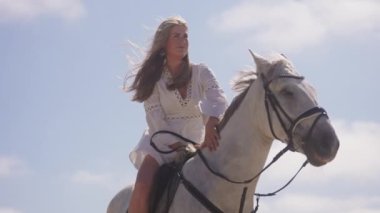 Beyaz elbiseli bir kızın güneşli bir günde beyaz atına dokunduğu orta boy bir fotoğraf.