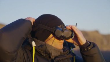 Ceket ve bere giyen bir adam İzlanda 'nın Reynisfjall Dağı yakınlarında kafasına FPV gözlüklerini takar ve ayarlar.