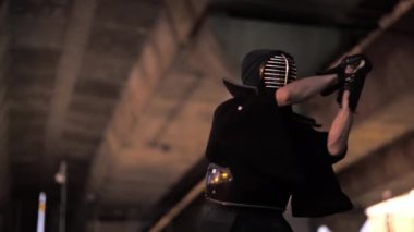 Geleneksel kendo üniforması giymiş bir adam, kılıcıyla caddeye vururken odaklanma ve yoğunluk yayar.