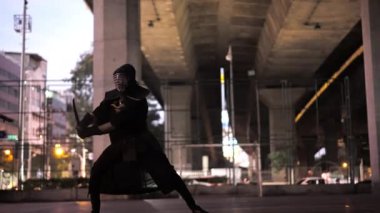 Kendo üniformalı bir adam dışarıda parıldayan kılıcıyla güçlü vuruşlar yapar.