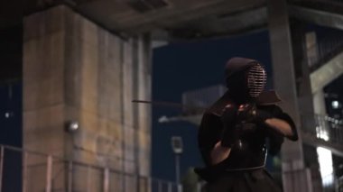 Kendo üniformalı bir adam gece vakti kılıç tekniği uyguluyor.