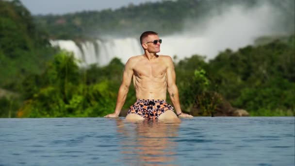 Ein Mann Badehose Und Dunkler Sonnenbrille Sitzt Rande Eines Pools — Stockvideo