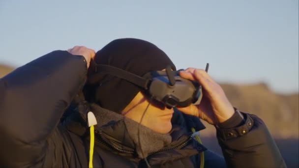 ジャケットとビーニーを着用し アイスランドのレイニス フィハール山近くの頭にFpvゴーグルを調整する男 — ストック動画