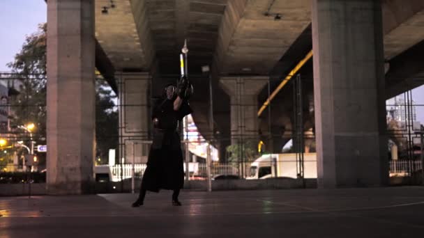剣道の制服を着た男は 夕暮れの間に忙しい通りに剣を振った — ストック動画