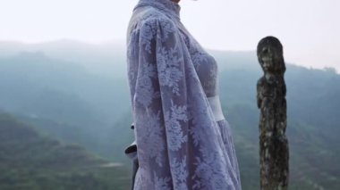 Lavanta dantelli bir elbise giymiş bir kadının yakın plan bir fotoğrafı, bir dağın kenarına doğru yürürken, mavi saat boyunca pirinç teraslarını gören bir kadın.