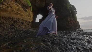 Deniz kıyısında esen güçlü rüzgarlara rağmen bir kadın zarif bir şekilde dans eder.