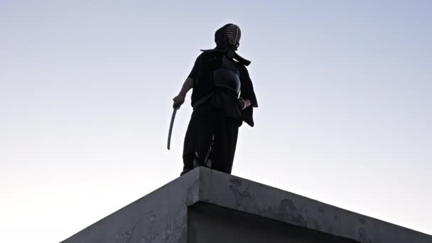 Bir Ninja Beton Bir Çatıda Duruyor Alacakaranlıkta Kılıcını Çıkarıyor — Stok video