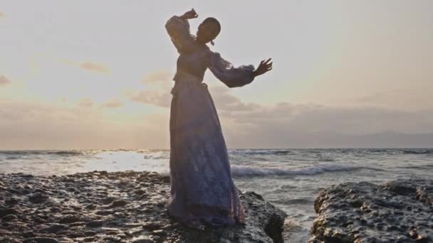 Kobieta Koronkowej Sukience Tańcząca Przed Słońcem Skalistym Wybrzeżu Rozbryzganymi Falami — Wideo stockowe