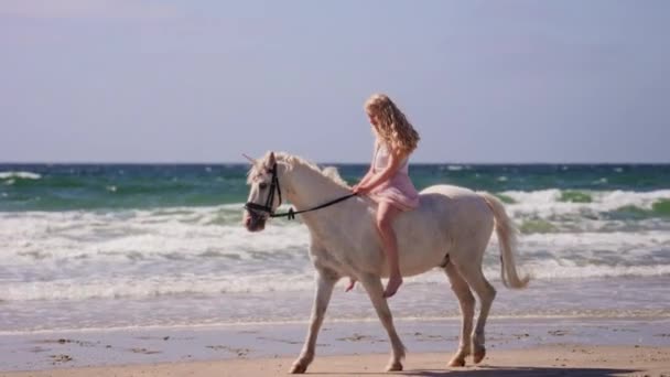 昼間の落ち着いた波でビーチでユニコーンを乗ってブロンドの女の子バックの広い側面のショット — ストック動画