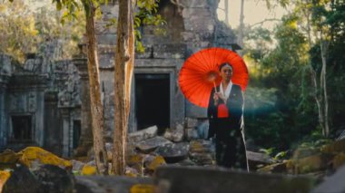 Siyah kimono giymiş, elinde kırmızı bir şemsiye tutan, yosun kaplı tapınağa bakan bir kadın.