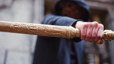 Terk edilmiş bir tapınakta, kapüşonlu bir adam tarafından kullanılan, altın kılıcın detaylı detaylarını gösteren yakın çekim.