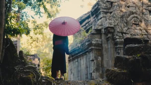 カンボジアの放棄された寺院のモチーフグラウンドに赤い傘を手に入れた黒い着物の女性のバックビューショット — ストック動画