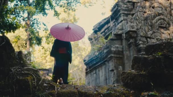 赤い傘を手にした黒い着物の女性のバックビューショットは 昼間のカンボジアの放棄された寺院に向かって歩きます — ストック動画