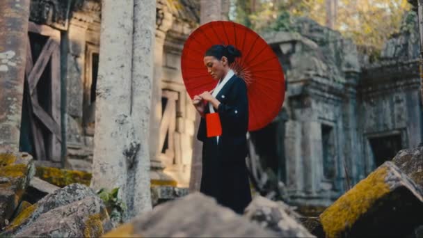 柬埔寨一名身穿黑色和服 头戴红色纸伞的妇女白天站在废弃的寺庙前朝下看 — 图库视频影像