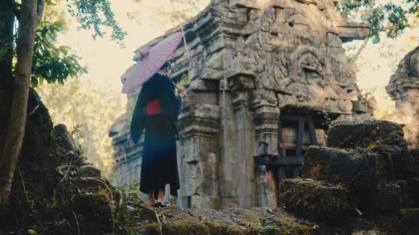黒い着物を着て 捨てられた寺院の遺跡のなかで赤い傘を抱いている女性 — ストック動画