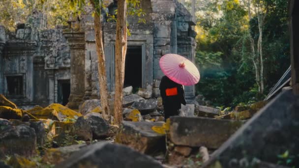 赤い紙の傘を手に持っている黒い着物の女性は 昼間にカンボジアで放棄された寺院を探検します — ストック動画
