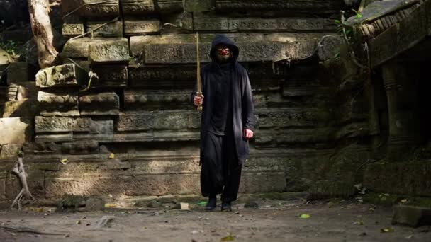 一个戴着哈曼面具的男人在白天拿着剑在布满青苔的庙宇里行走的全景 — 图库视频影像