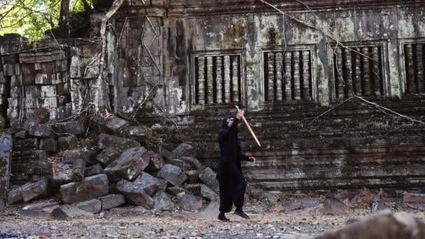 一个戴著哈曼恶魔面具的蒙面男子的宽幅照片 他拿着金色的剑在荒芜的庙宇废墟上翻身 — 图库视频影像