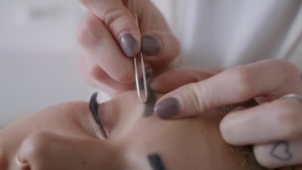 彼女の眉毛を持つ女性のクローズアップは 金属のツイーザーのペアでサロンに摘み取りました — ストック動画