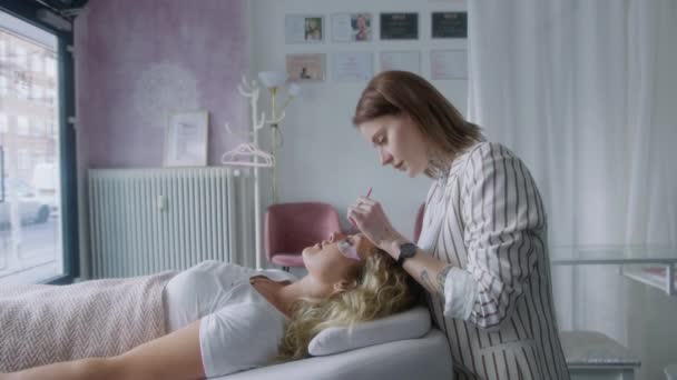 一个女人躺在床上放松 而一个熟练的美容师在沙龙里用睫毛做伸展手术 — 图库视频影像
