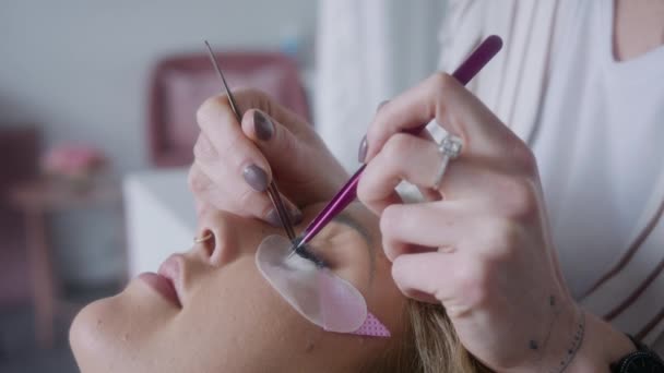 一位专业美容师的特写镜头 她在客户身上用金属镊子仔细地应用睫毛扩展程序 — 图库视频影像