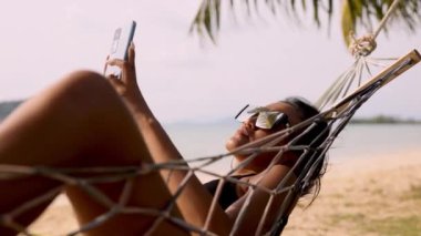 Koh Mak 'ın sakin sahillerinde hamakta olan bir kadın, doğanın güzelliği ile çevrili iken telefonla dünyayla bağlantı kuruyor.