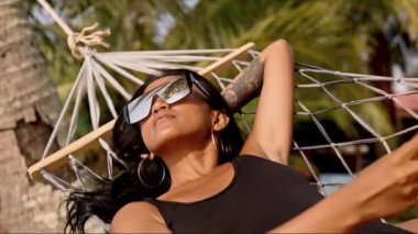 Bir kadın, Tayland 'ın Koh Mak plajındaki bir hamakta dinlenirken telefonuna bakar.