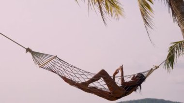 Bir bayan, Koh Mak 'ta bir plajda telefonuyla bağlı kalırken hamakta vakit geçirmekten zevk alır.