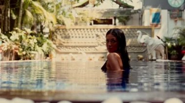 Havuzdaki çarpıcı bir kadın, yoğun bakışlarıyla kamerayı cezbediyor. Suyun altında kendine güveni ve cazibesi yayılıyor.