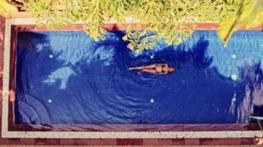 Parlak gün ışığında, havuzun yüzeyinde huzur içinde yüzen bir kadın huzurlu ve rahatlatıcı bir huzur anını somutlaştırıyor.