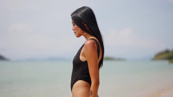 マックの元のビーチの海岸で洗練された黒い水着のエレガントな女性は 楽園の背景に対する洗練を体現しています — ストック動画