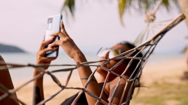 ソーシャルメディアを通じてデジタル世界とつながるビーチハンモックの女性 — ストック動画