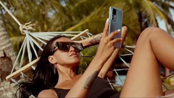 一个女人在Koh Mak的原始海滩旁的吊床上享受着欢乐的社交媒体休息 — 图库视频影像