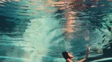 Beyaz mayo giyen bir bayan ferahlatıcı havuz suyuna dalmışken poz verir.