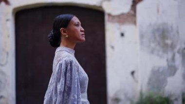 Şık bir çörek saç stili ve güzel bir leylak elbise giyen zarif bir kadın Vigan 'ın resimli caddelerinde geziniyor, sonsuz bir zarafet yayıyor.