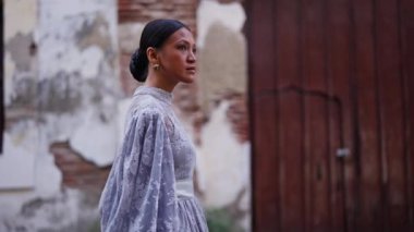 Şık bir çörek saç stili olan ve leylak rengi bir elbise giyen bir kadın Vigan 'ın büyüleyici caddelerinde zarif bir şekilde geziniyor.