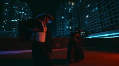 Usta bir erkek ve kadın Kung Fu 'daki ustalıklarını gösteriyorlar. Düzgün hareketleri ve doğru teknikleri arkalarındaki şehir siluetiyle mükemmel uyum içinde.