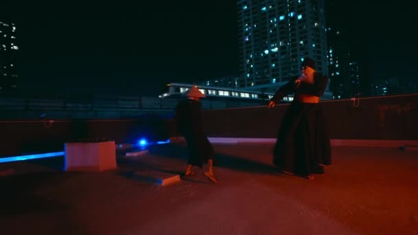 屋上のダイナミックなカンフーセッションに参加する熟練した男女が 都市風景を背景に印象的な武道の動きを示しています — ストック動画
